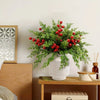 A vase filled with artificial Christmas berry stems and pine branches on a wooden table.