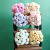 A display of silk peony bouquets in shades of pink, cream, and lavender arranged on wooden tiers.