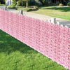 A long privacy fence screen made of pink artificial cherry blossoms borders a green lawn.