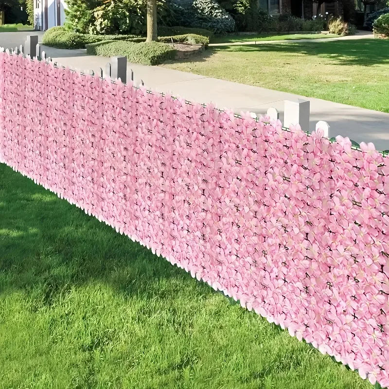 A long privacy fence screen made of pink artificial cherry blossoms borders a green lawn.