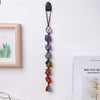 A dark brown crystal chakra rolling stone pendant suspended by a leather cord, displayed next to a framed picture.