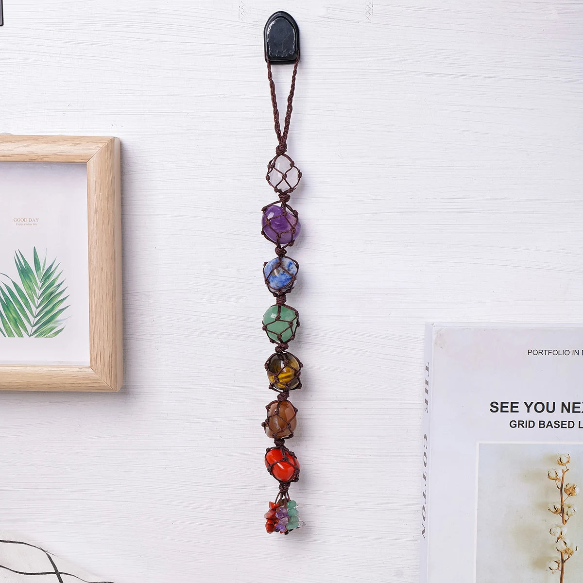 A dark brown crystal chakra rolling stone pendant suspended by a leather cord, displayed next to a framed picture.