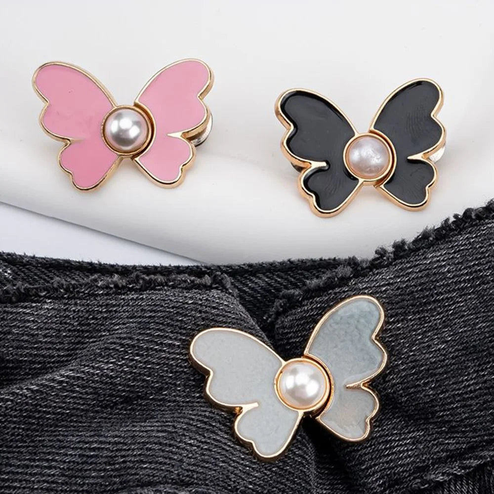 A set of three pearl butterfly buttons in pink, black, and silver are shown against a dark denim background.