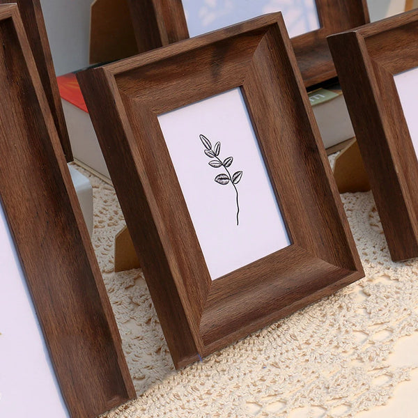 A set of dark brown wooden photo frames with white mats and simple botanical line art displayed on a light textured surface.
