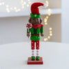 A handcrafted wooden nutcracker soldier figurine dressed in a green uniform and red hat standing on a red base.