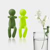 A set of three human-shaped plant supports in shades of green and lime yellow, displayed next to a glass of water.