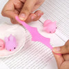 A hand holds a pink mini cartoon animal stress relief toy against a sheet of graph paper.