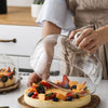 A glass dome cover is placed over a cake tray, showing a round cake decorated with fresh fruit.