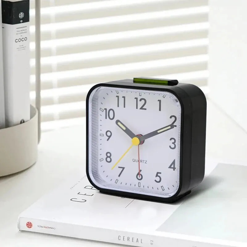 A black digital alarm clock with a white face and green accents sits on a white surface.