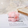 A set of two pink cube soy wax candles resting on a white notebook next to a sheer fabric.