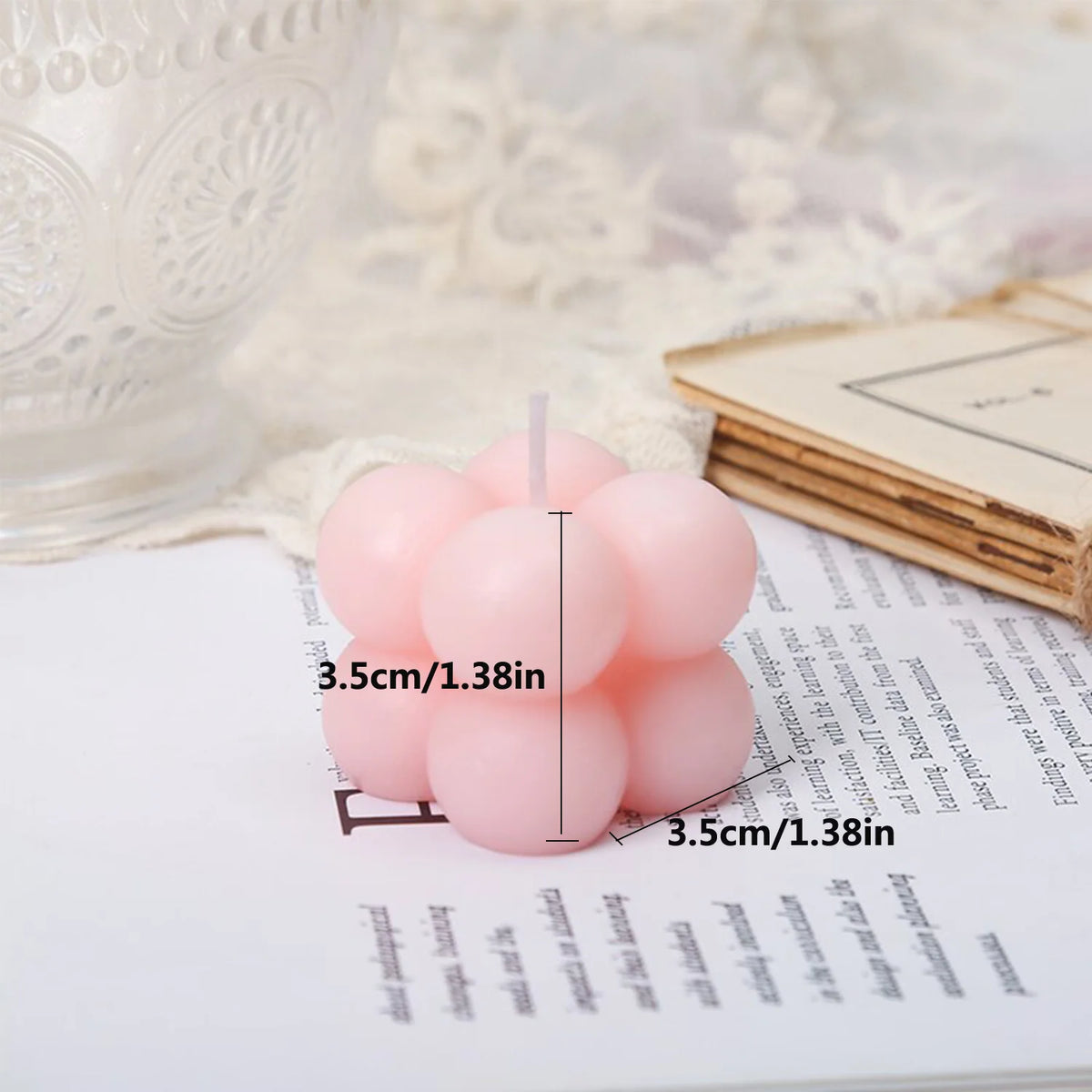 A set of two pink cube soy wax candles resting on a white notebook next to a sheer fabric.