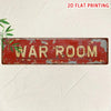 A distressed red metal tin sign with the words WAR ROOM painted in gold lettering on a light background.
