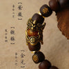 A close-up of a handcrafted Thunder-Wood Pixiu bracelet featuring semi-jade beads and an ornate gold-colored charm.