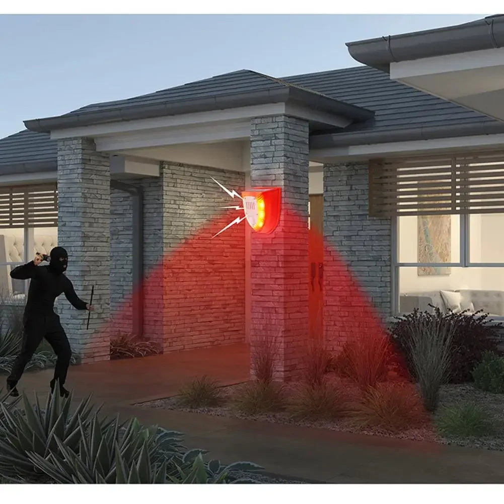 A solar-powered motion sensor alarm system with a flashing red siren illuminating a house facade.