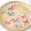 A collection of 3D embroidered butterfly patches in various shades of pink, purple, and green are displayed on a woven bamboo