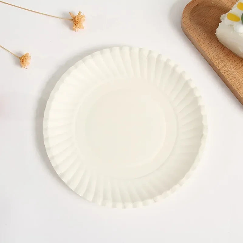 A white fluted paper plate is centered on a white surface next to a wooden board.