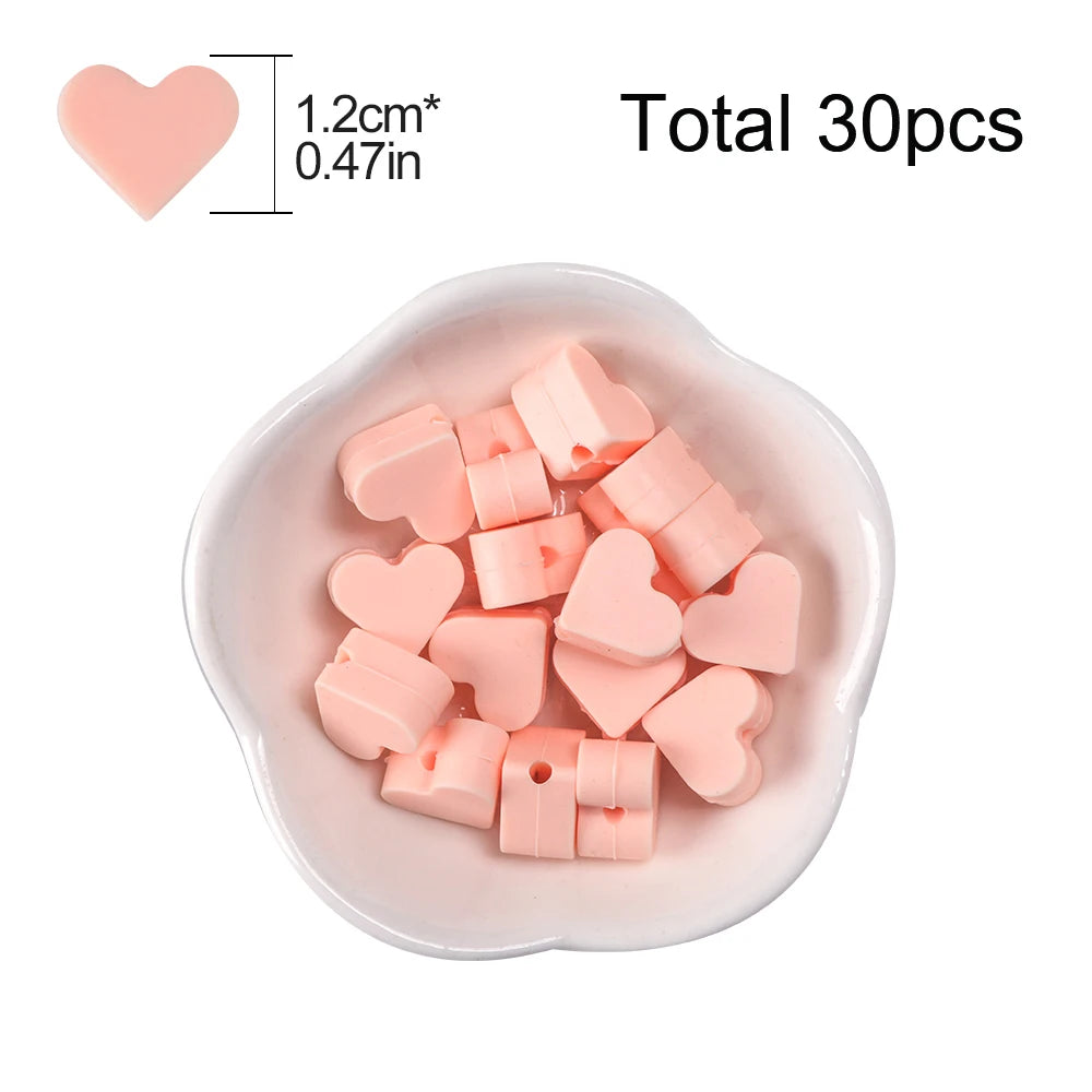 A collection of 30 pink silicone heart beads in various shapes and sizes displayed in a white dish.