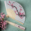 A hand carved bamboo folding fan with light gray and pink stripes and black branches with pink blossoms.