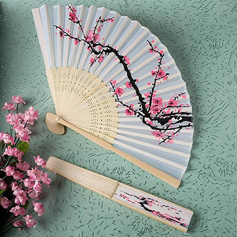 A hand carved bamboo folding fan with light gray and pink stripes and black branches with pink blossoms.
