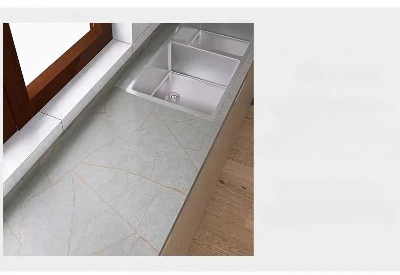 A kitchen countertop featuring a stainless steel sink set into a light marble surface.