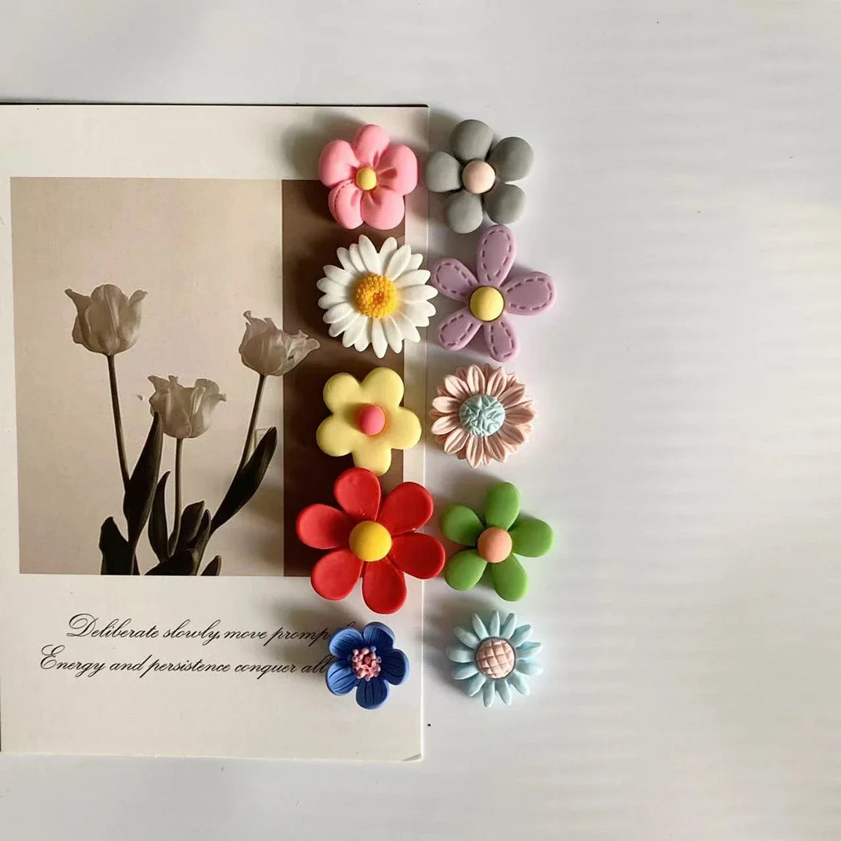 A collection of colorful felt flower magnets arranged on a white card next to a photo.