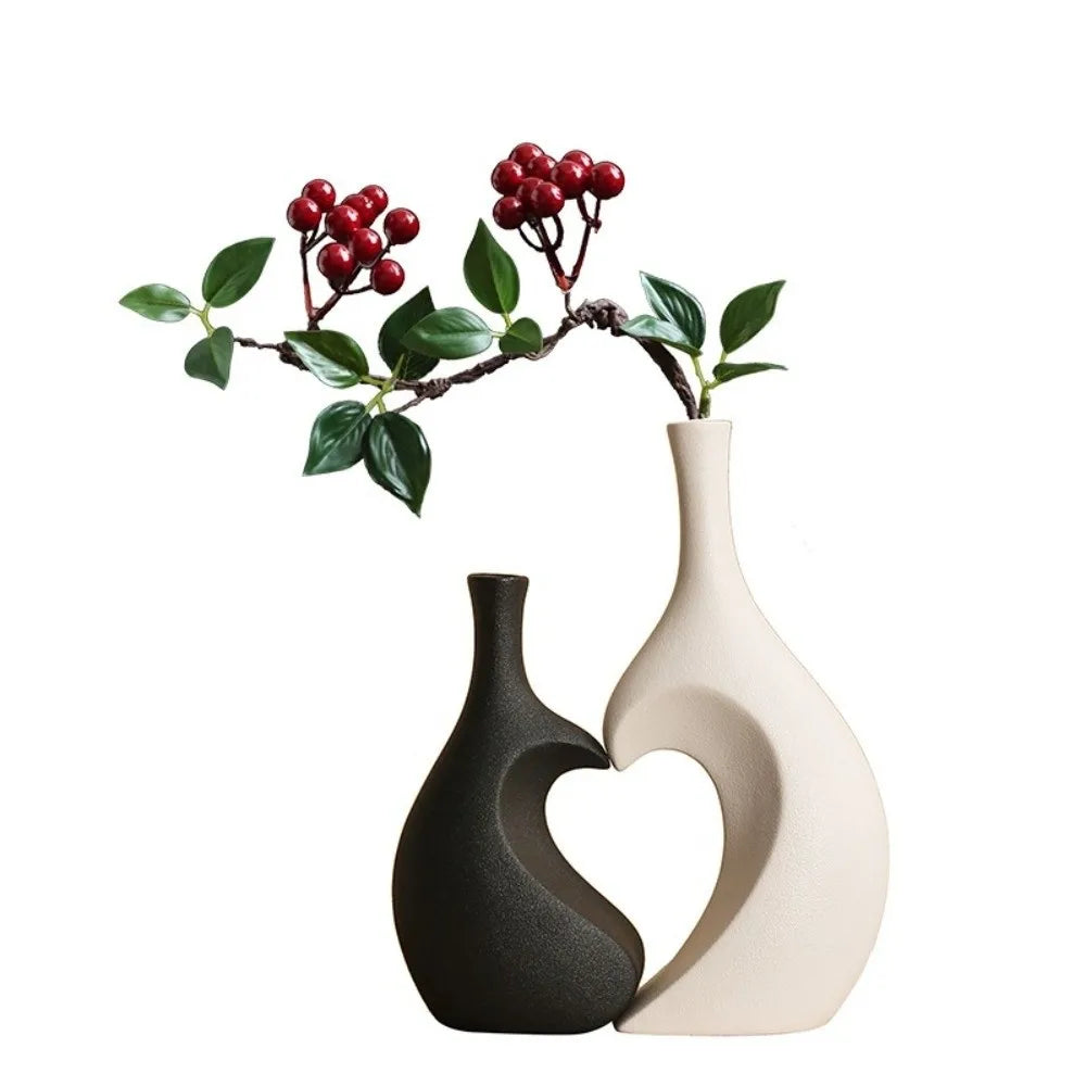 Modern heart-shaped ceramic vase with a matte black and beige finish, decorated with red berries and green leaves.