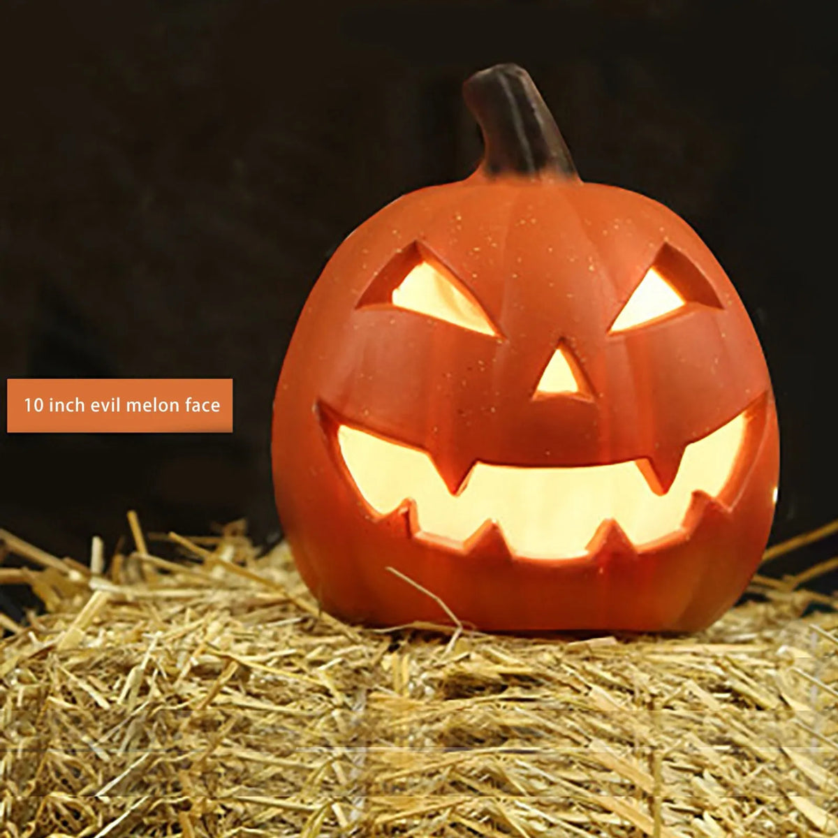 Calabaza de cerámica naranja tallada con cara amenazadora, iluminada desde dentro, sobre paja.