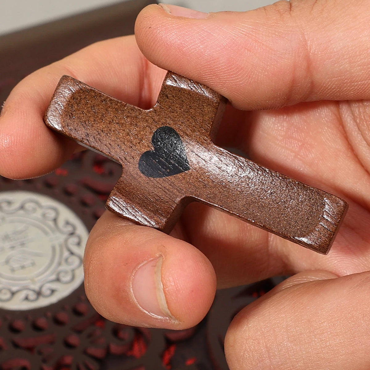 A hand holds a small, dark brown wooden cross with a carved heart shape for prayer and reflection.