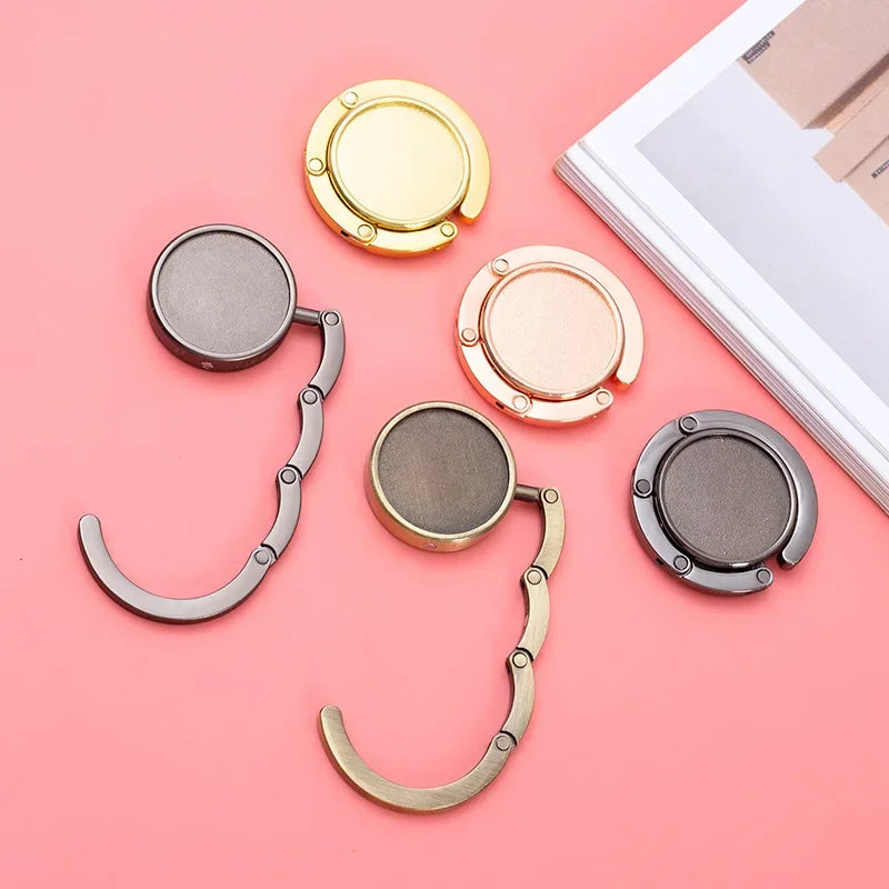 A set of gold and silver compact folding table bag hooks and purse hangers displayed on a pink background.