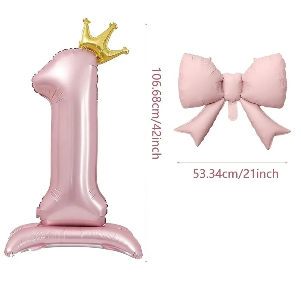 A pink foil balloon shaped like the number one with a gold crown topper and a pink bow.