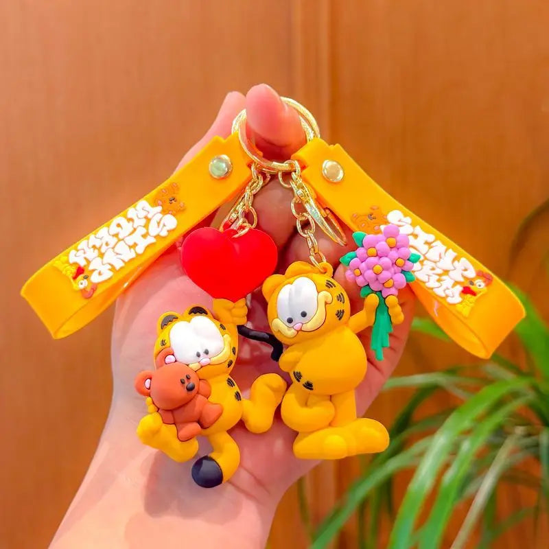 A hand holds a yellow keychain pendant featuring Garfield cartoon characters and a red heart.