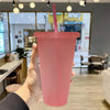 A hand holds a pink glitter party cup with a straw and lid in a bright indoor setting.