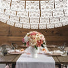 Blumenschmuck mit rosa und weißen Rosen auf rustikalem Holztisch mit weißem Papel-Picado-Banner im Hintergrund