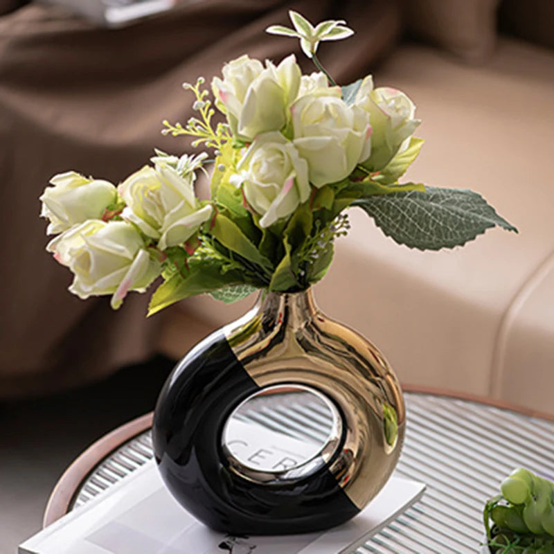 A bouquet of white roses in a glossy black and gold ceramic vase on a glass table.