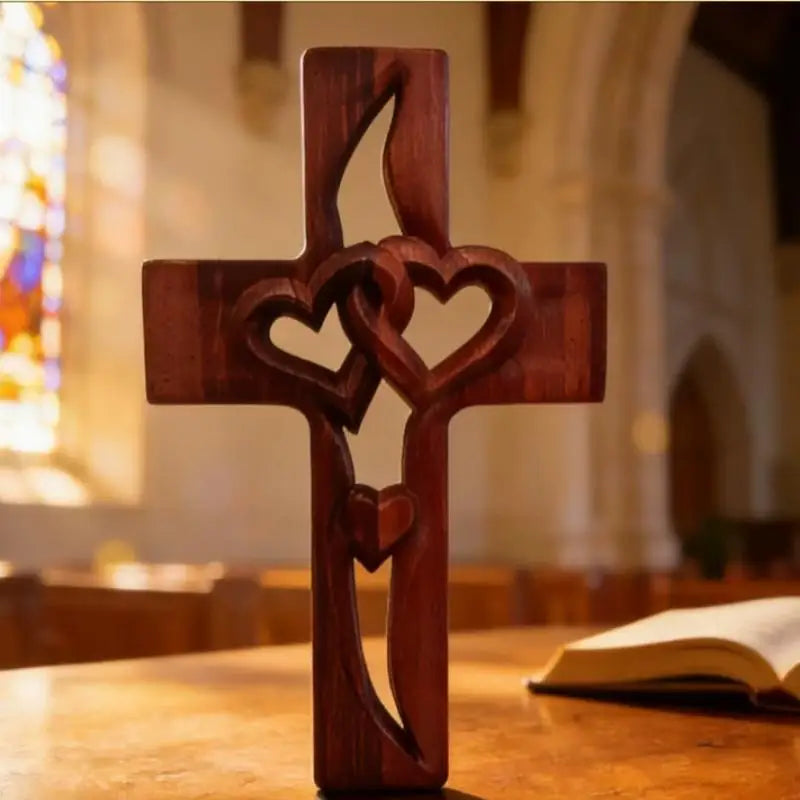 A wooden cross carved with intertwined hearts resting on a wooden surface in a church setting.