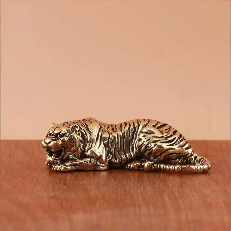 A vintage brass tiger figurine statue lying on a wooden surface.