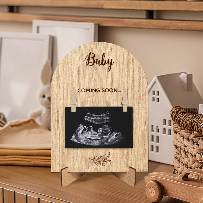 A wooden photo frame with the word Baby and Coming Soon on it, displayed on a wooden shelf.
