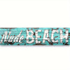 A weathered teal wooden sign with the words NUDE BEACH painted in distressed white lettering.