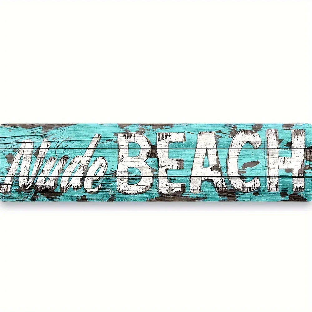 A weathered teal wooden sign with the words NUDE BEACH painted in distressed white lettering.
