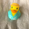 A yellow rubber duck bath toy with an orange beak and a yellow hat sitting on a silver textured surface.