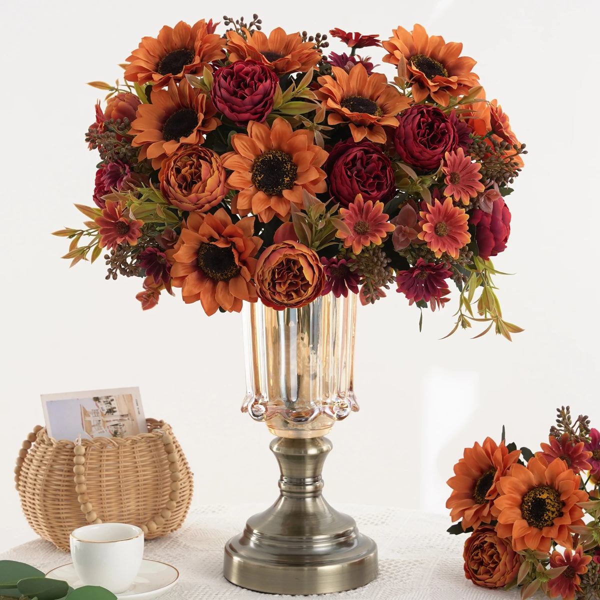 Un arrangement de tournesols artificiels et de pivoines rouge foncé dans un vase en verre.