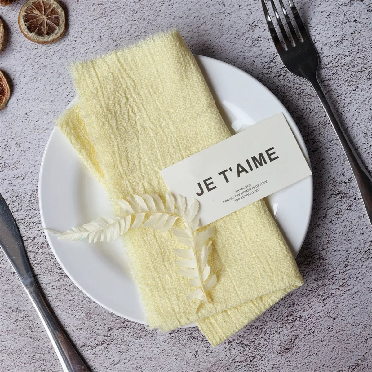 A set of ten yellow handcrafted fringed cotton napkins is displayed on a white plate with a tag that reads Je t'aime