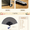 A dark blue patterned folding hand fan with a black handle and purple tassel.