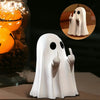 A white ghost figurine with a sassy hand gesture is shown next to a glass jar filled with orange lights and pinecones.