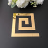 A gold acrylic mirror wall sticker in a spiral design is placed on a dark surface with white flowers in the background.