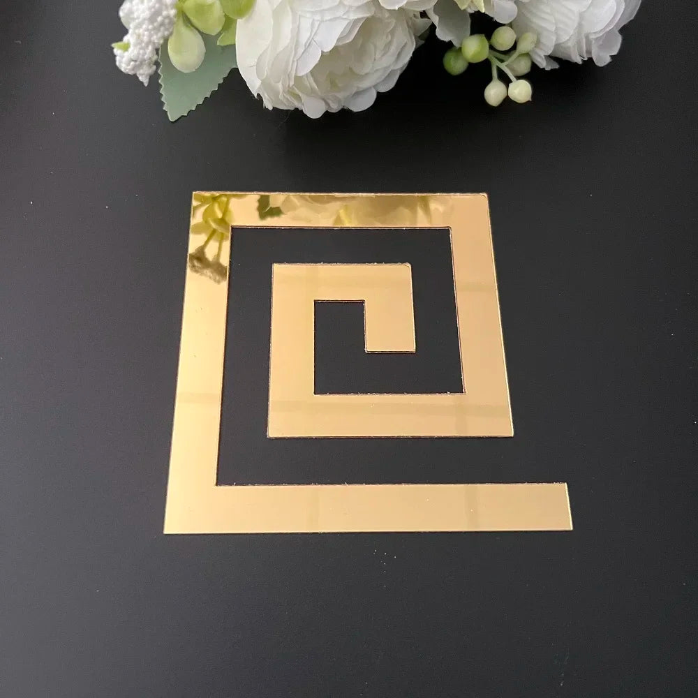 A gold acrylic mirror wall sticker in a spiral design is placed on a dark surface with white flowers in the background.