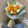 A bouquet of handmade crochet tulip flowers in shades of yellow and orange, wrapped in light green paper.