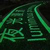 A dark path is illuminated by bright green glow-in-the-dark pebbles with Japanese and English text on the ground.