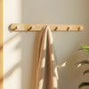 A light wood wall hook rack with four circular hooks mounted on a beige wall, featuring a folded tan towel.