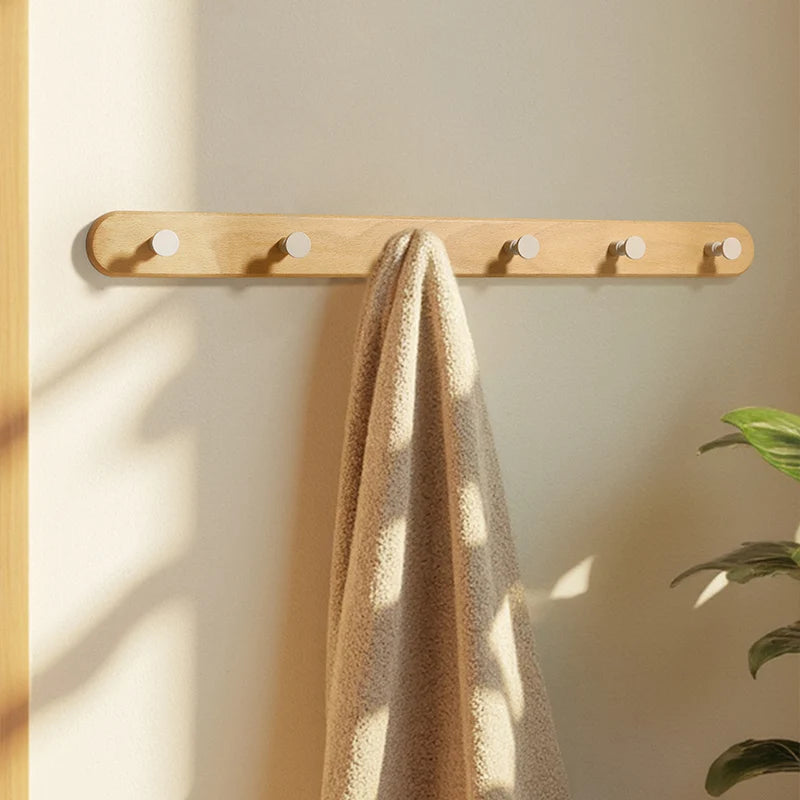 A light wood wall hook rack with four circular hooks mounted on a beige wall, featuring a folded tan towel.